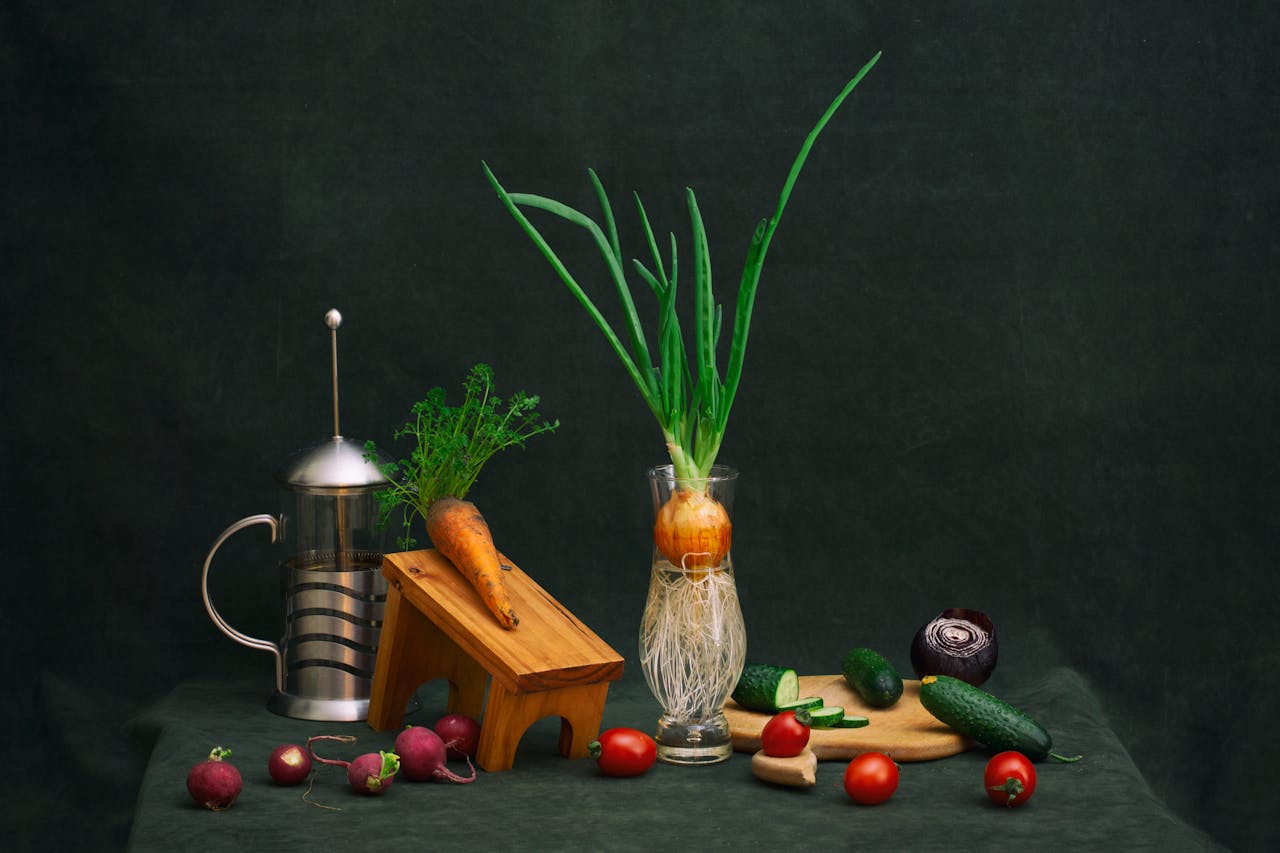 A creative still life featuring vegetables and a French press on a wooden table.